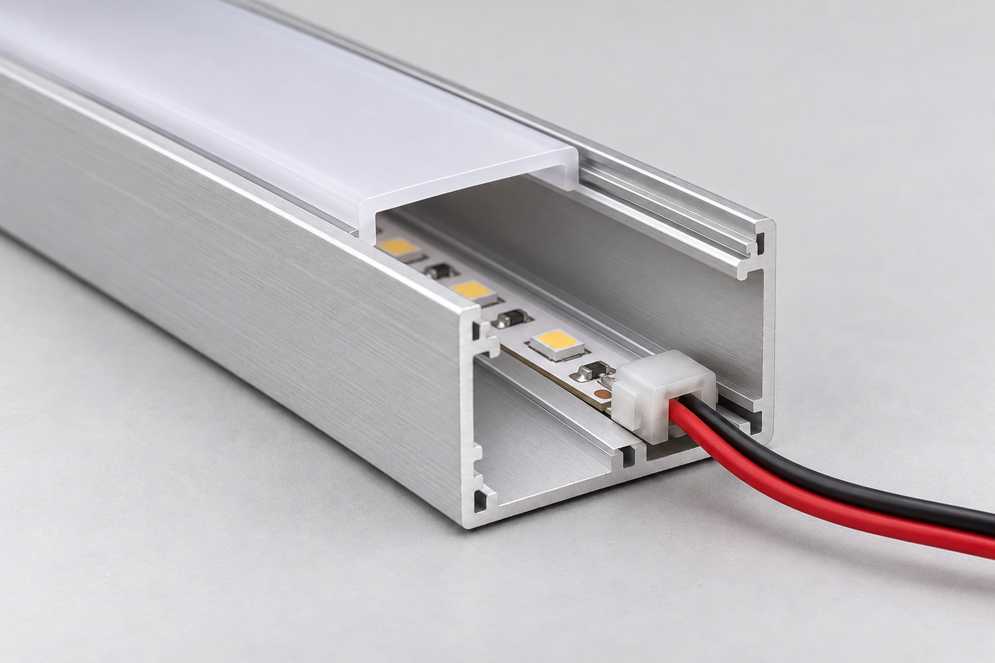 Open aluminum profile showing an LED strip, an end connector and red and black wires inside the channel.