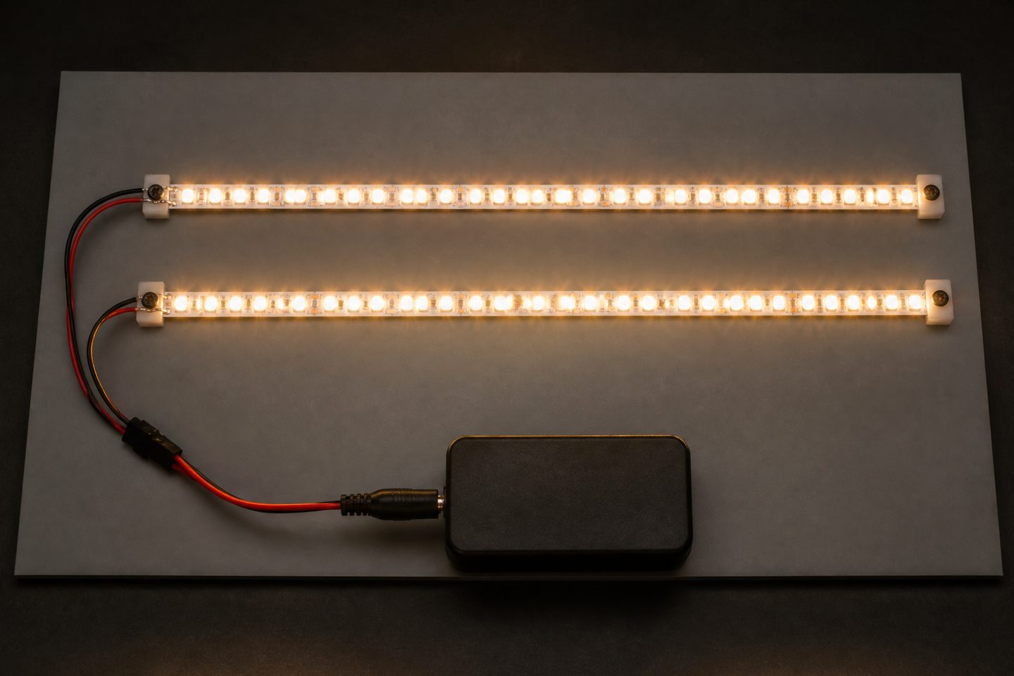 Two lit LED strips mounted parallel on a gray board and powered by the same supply.