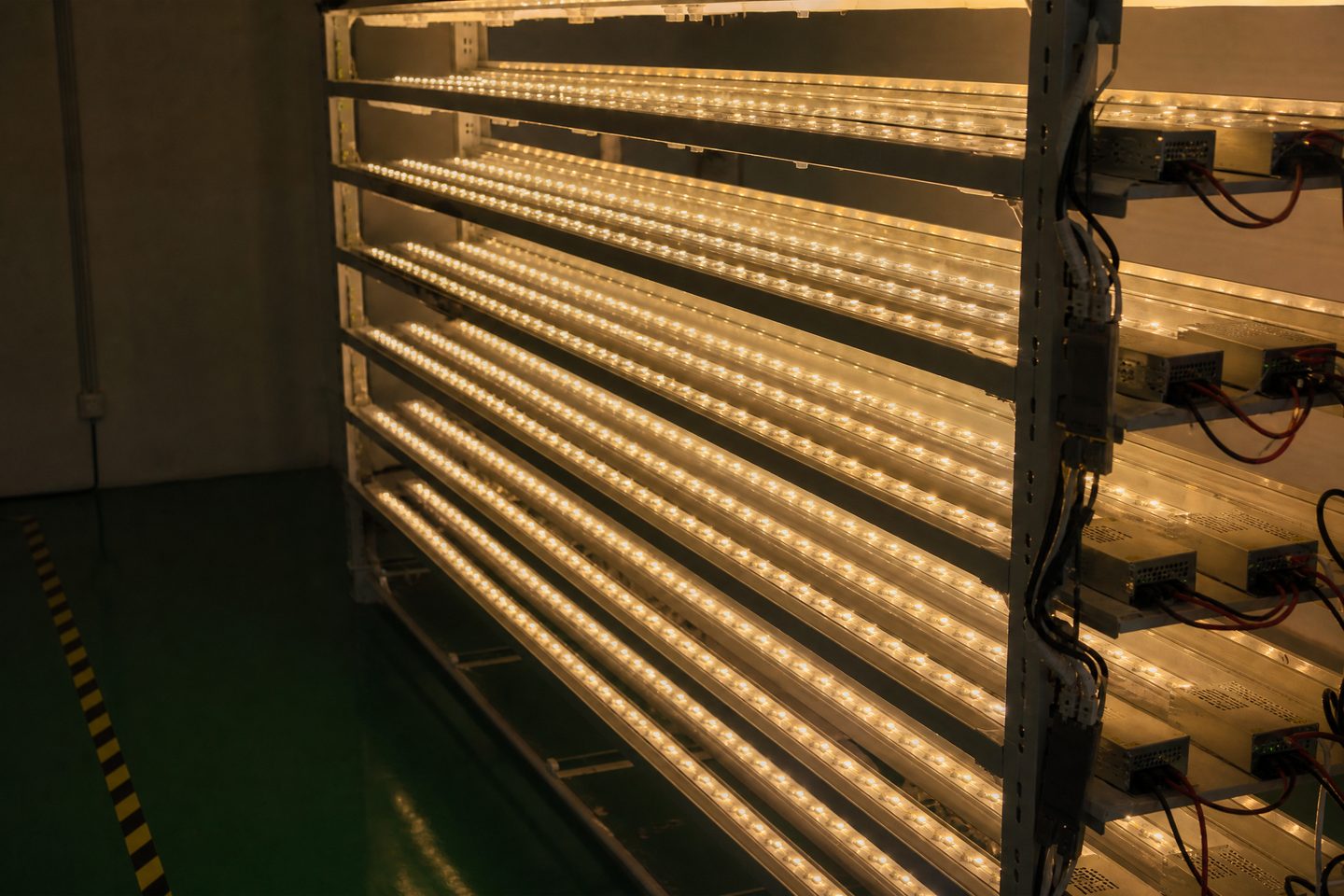Factory rack with many lit LED strips running a burn-in test, wired to power supplies.