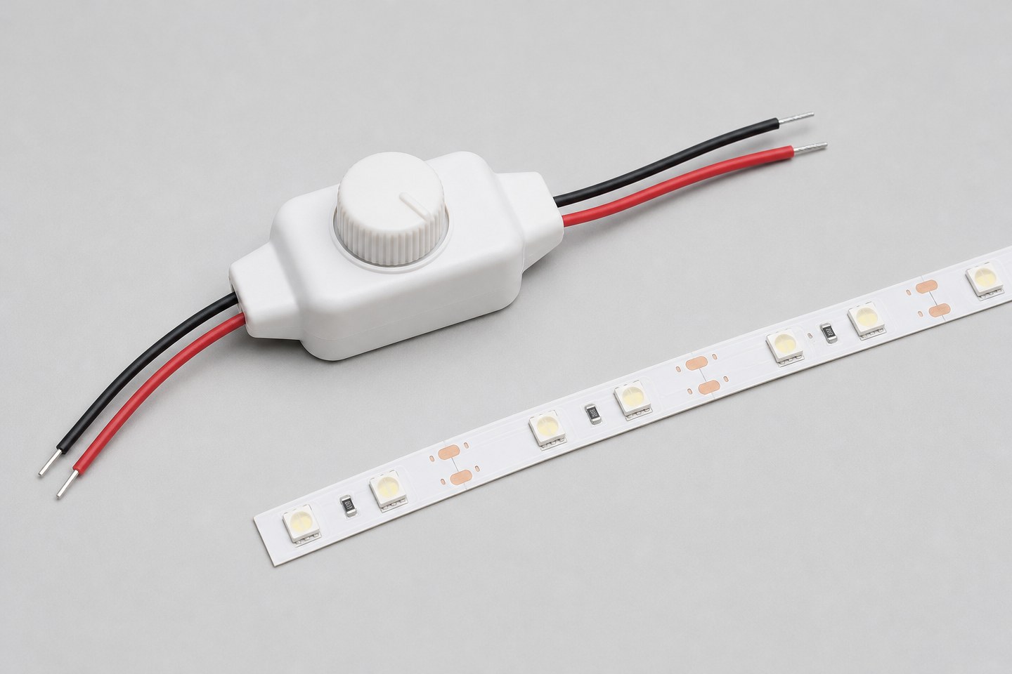 A small handheld dimmer controller module beside a short unlit LED strip segment.