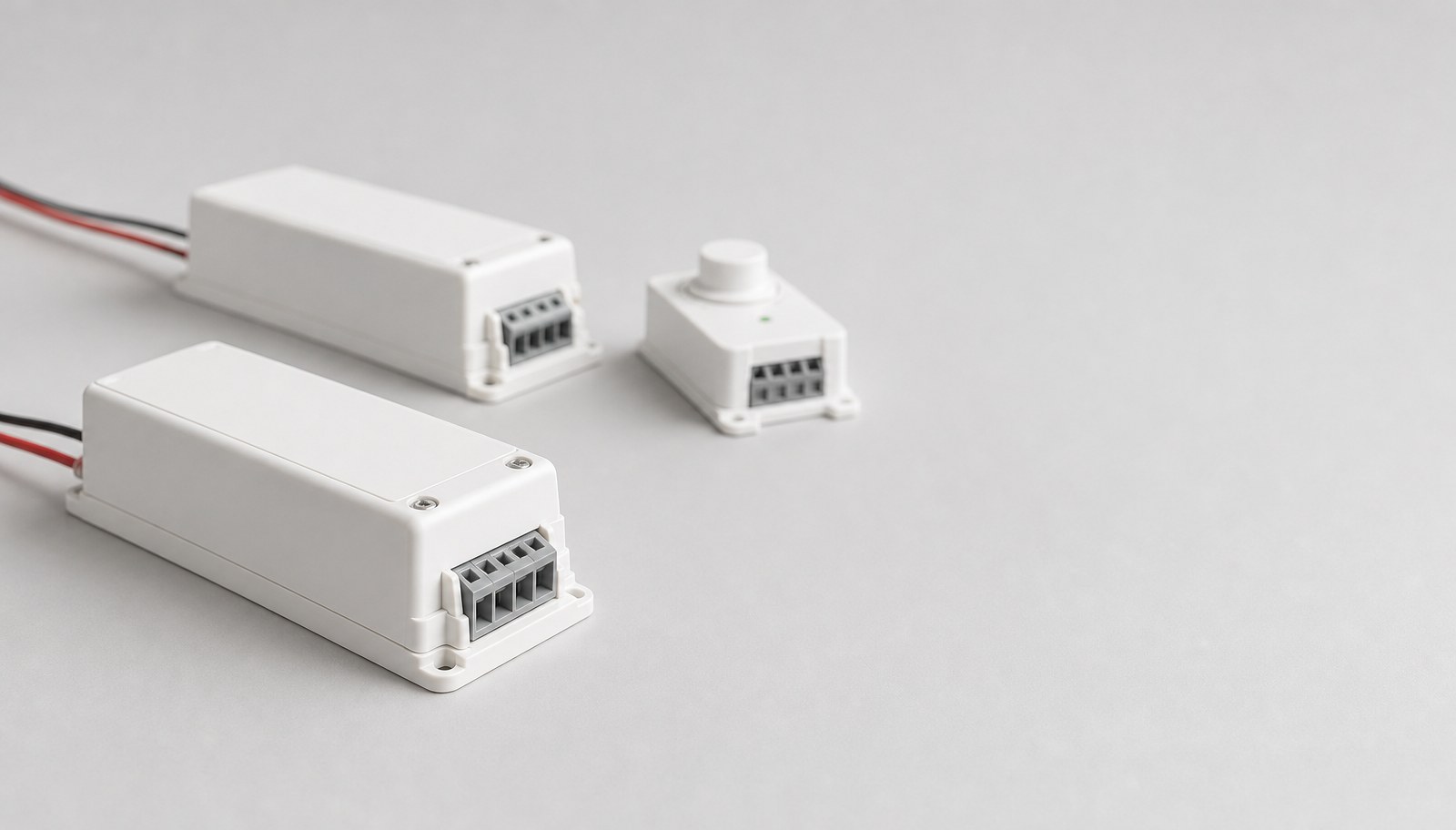 Two white LED driver units with wire leads on a gray studio surface, a small dimmer module beside them.