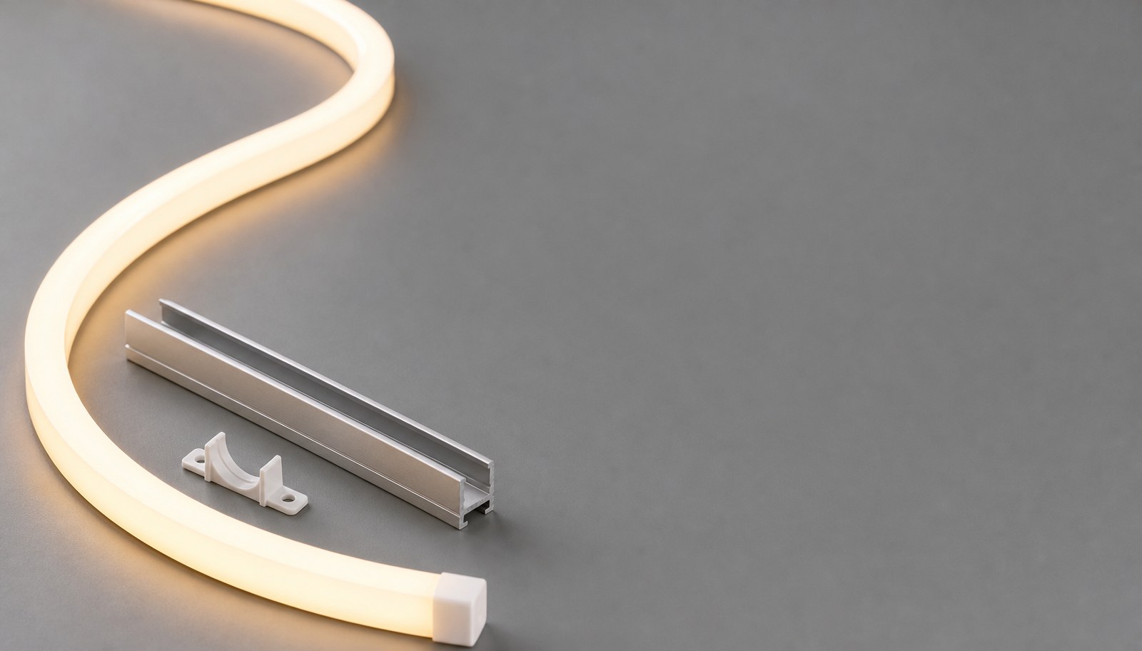 A length of warm-white illuminated LED neon flex curved on a gray surface beside an aluminum mounting channel.