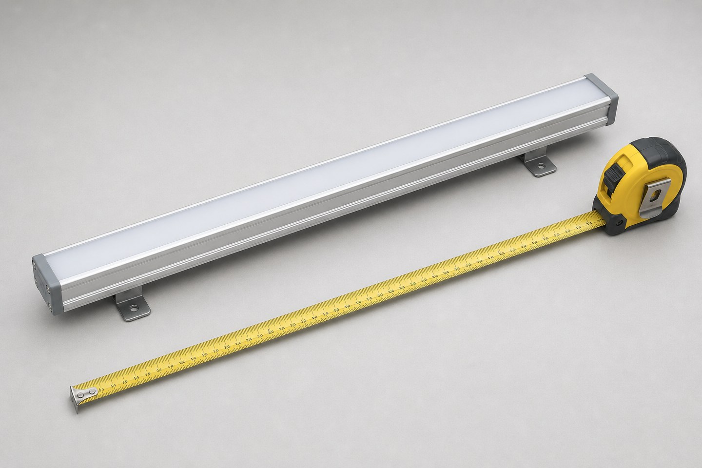 A rigid aluminum LED light bar being measured with a tape measure on a workbench.