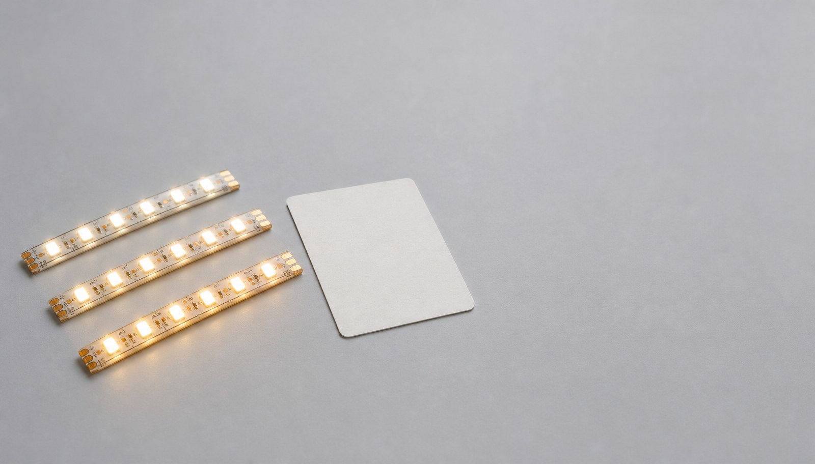 Three LED strip sample pieces of slightly different warm-white tones laid in a row on a gray surface.