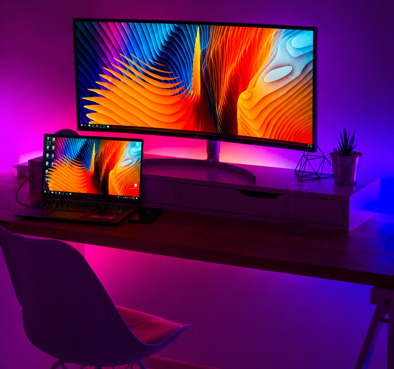 Purple and blue accent lighting behind a monitor and laptop desk.