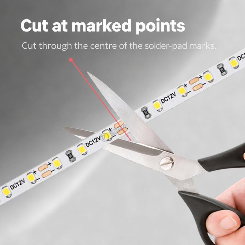 Scissors aligned with the marked solder pads on a 12 V strip.